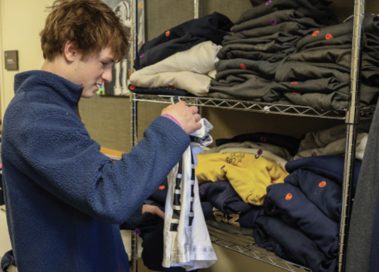 LOST AND FOUND Junior Fox Gottlich sorts through different student’s sweatshirts, hoodies, shorts and more on racks in the lost and found as he looks for a lost item of his own.