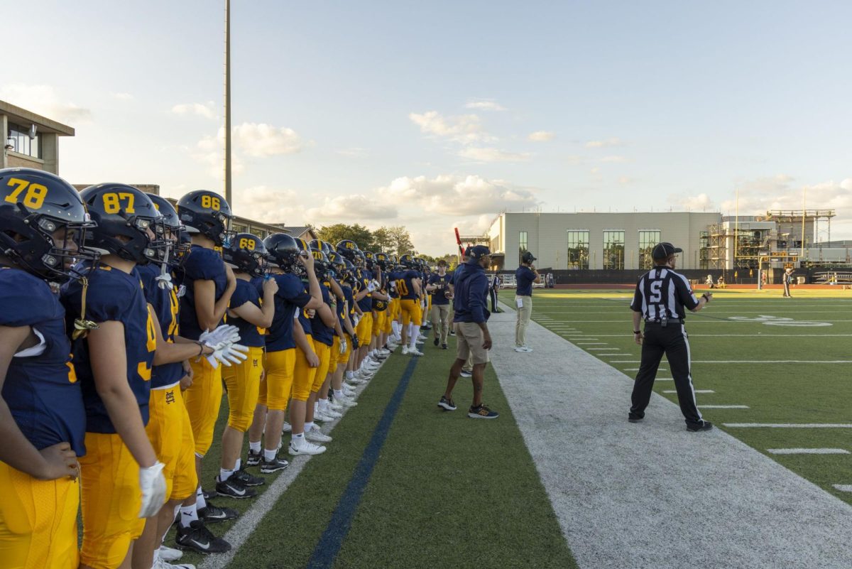 Football players look on to the field with the sky radiating in the background. 