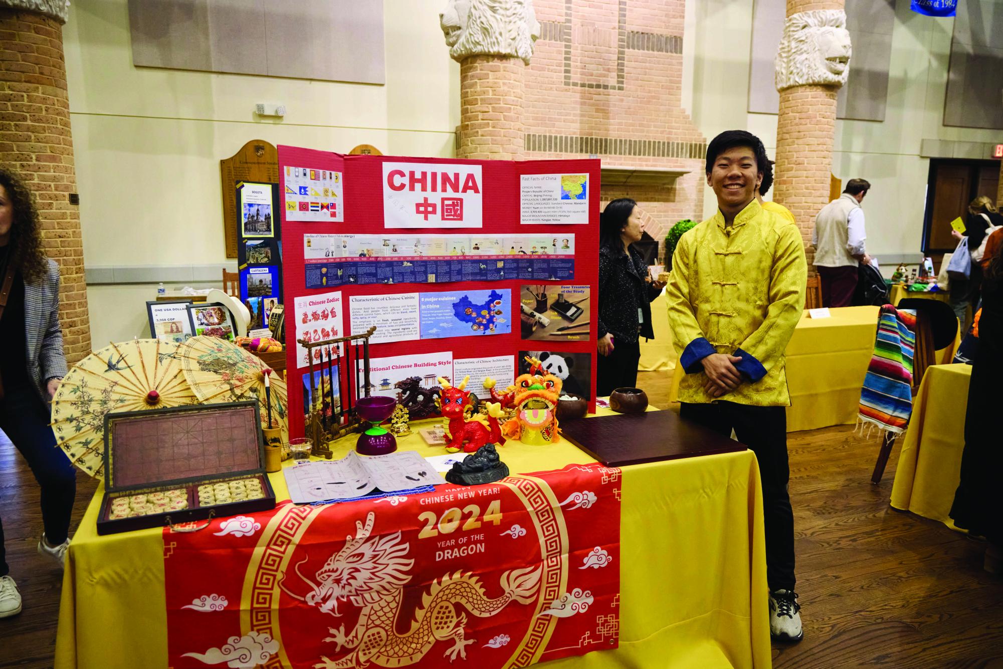 Senior Andrew Jin stands by the Chinese table, filled with traditional items and a poster board.