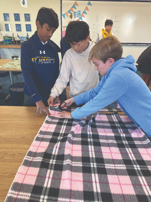 Club members huddle around a table while making scarves for the homeless
