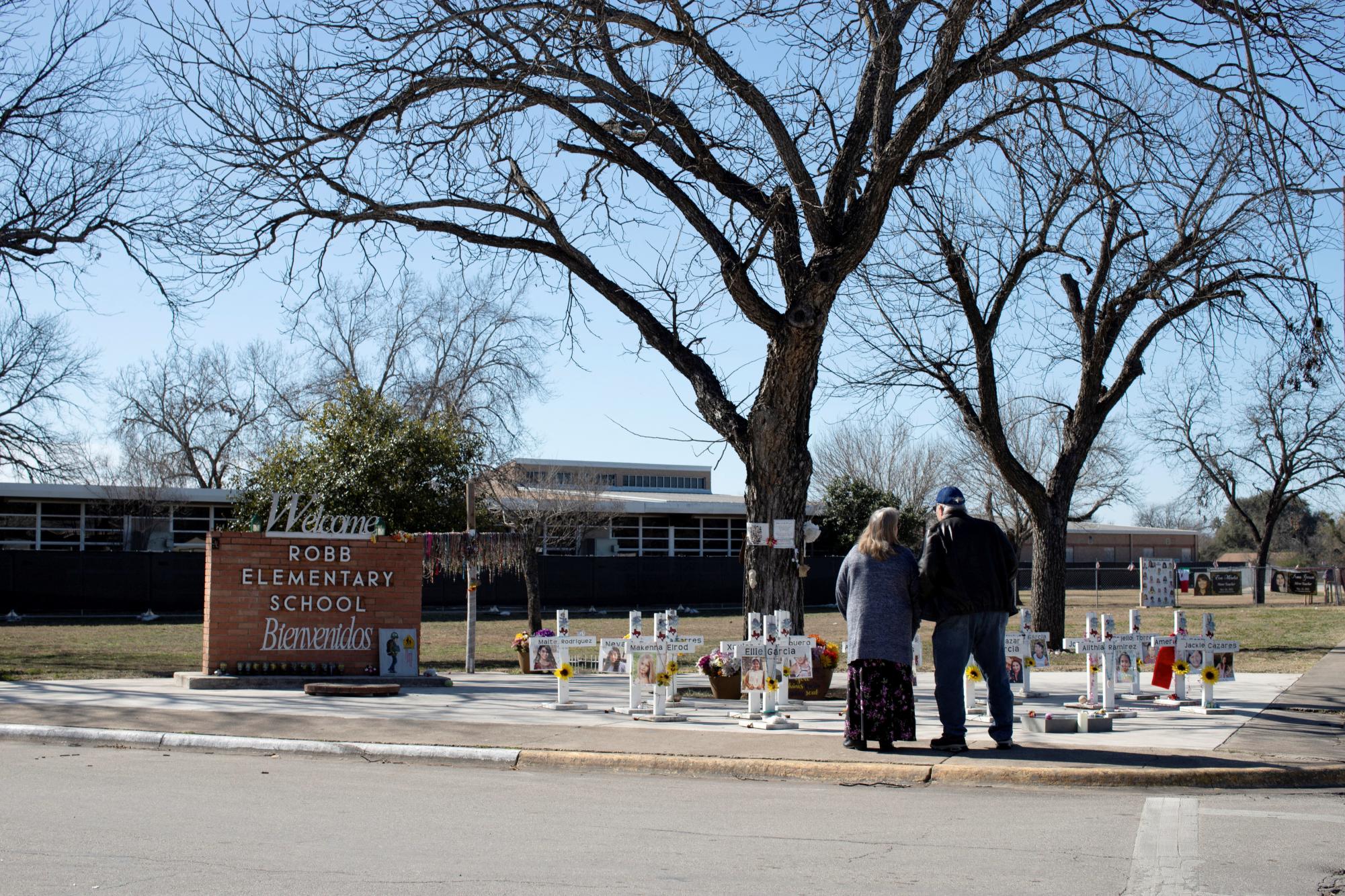 A couple visits memorial crosses in front of Robb Elementary School after a school shooting. 